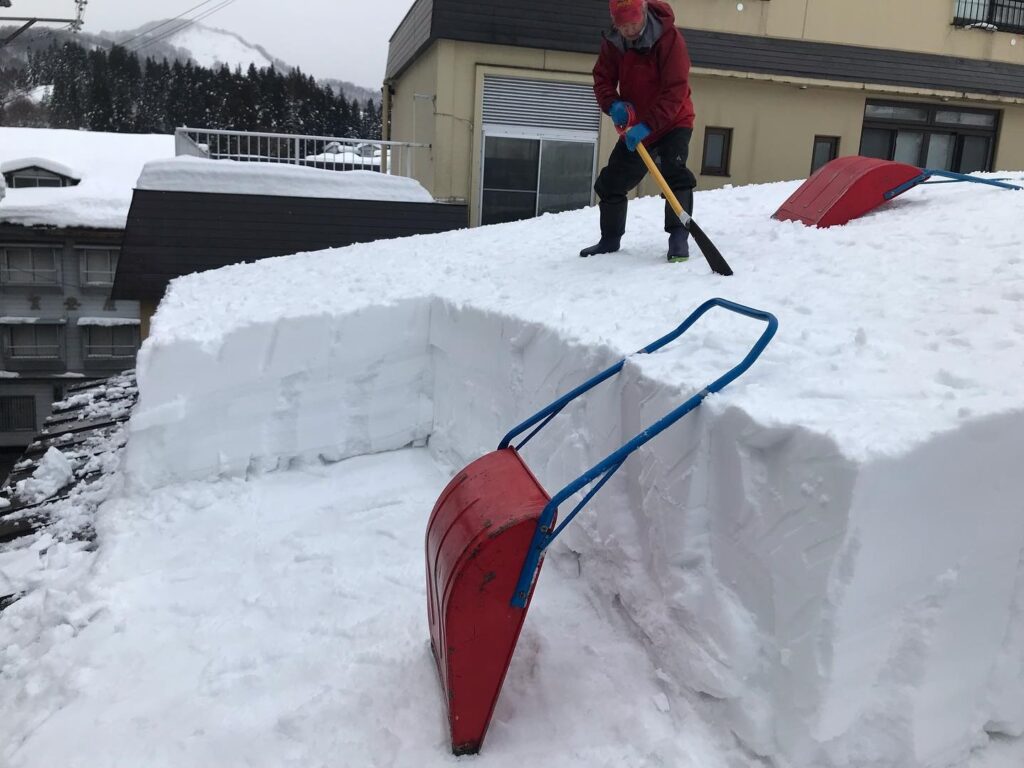 旅館の屋根に登り、雪下ろしをする姿